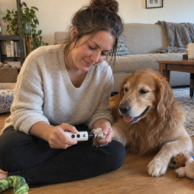 A customer holding the hair remover, coated in golden retriever hair, with her dog beside her on the sofa